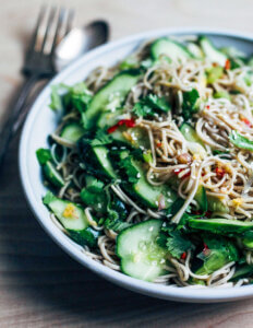 A bowl of soba noodle salad with cucumbers