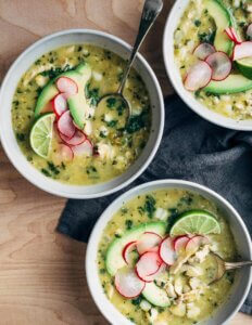 Bowls of chicken pozole soup with sliced avocado and radishes.