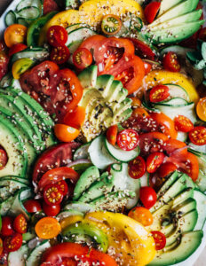 A close view of sliced avocados and tomatoes scattered with sesame seeds.