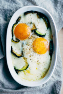 A baking dish with baked eggs, sliced zucchini, and melted mozzarella.