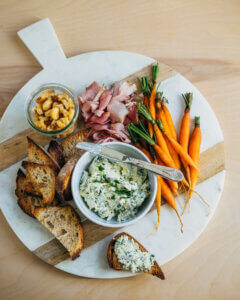 A serving platter with green pimento cheese, veggies, cured meat, and toasts.