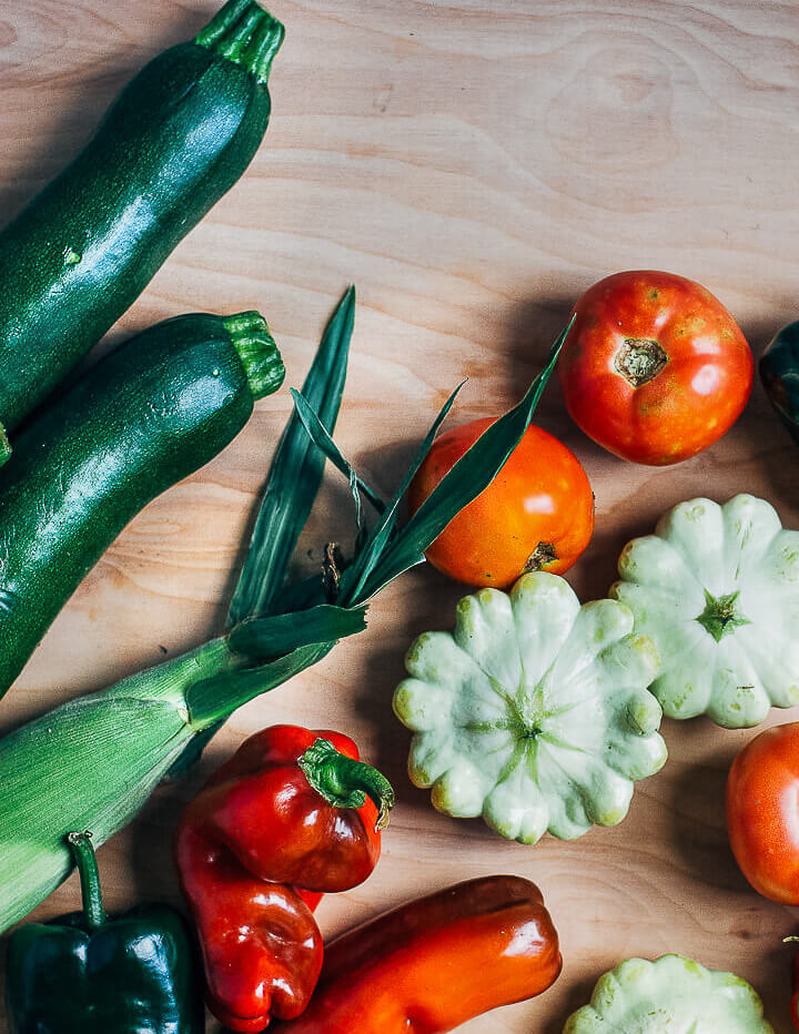 Zucchini, corn, peppers, patty pan squash, and tomatoes on a table top