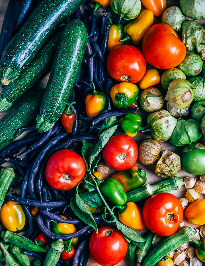 A table covered with zucchini, tomatoes, tomatillos, peppers, and okra. 