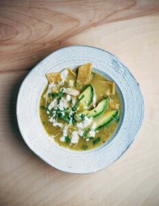 A bowl of tomatillo soup with avocados, tortilla strips, and vegan crema on top.