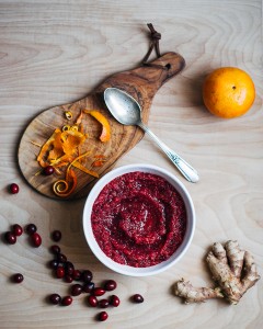 A bowl of cranberry relish surrounded by orange zest and ginger.