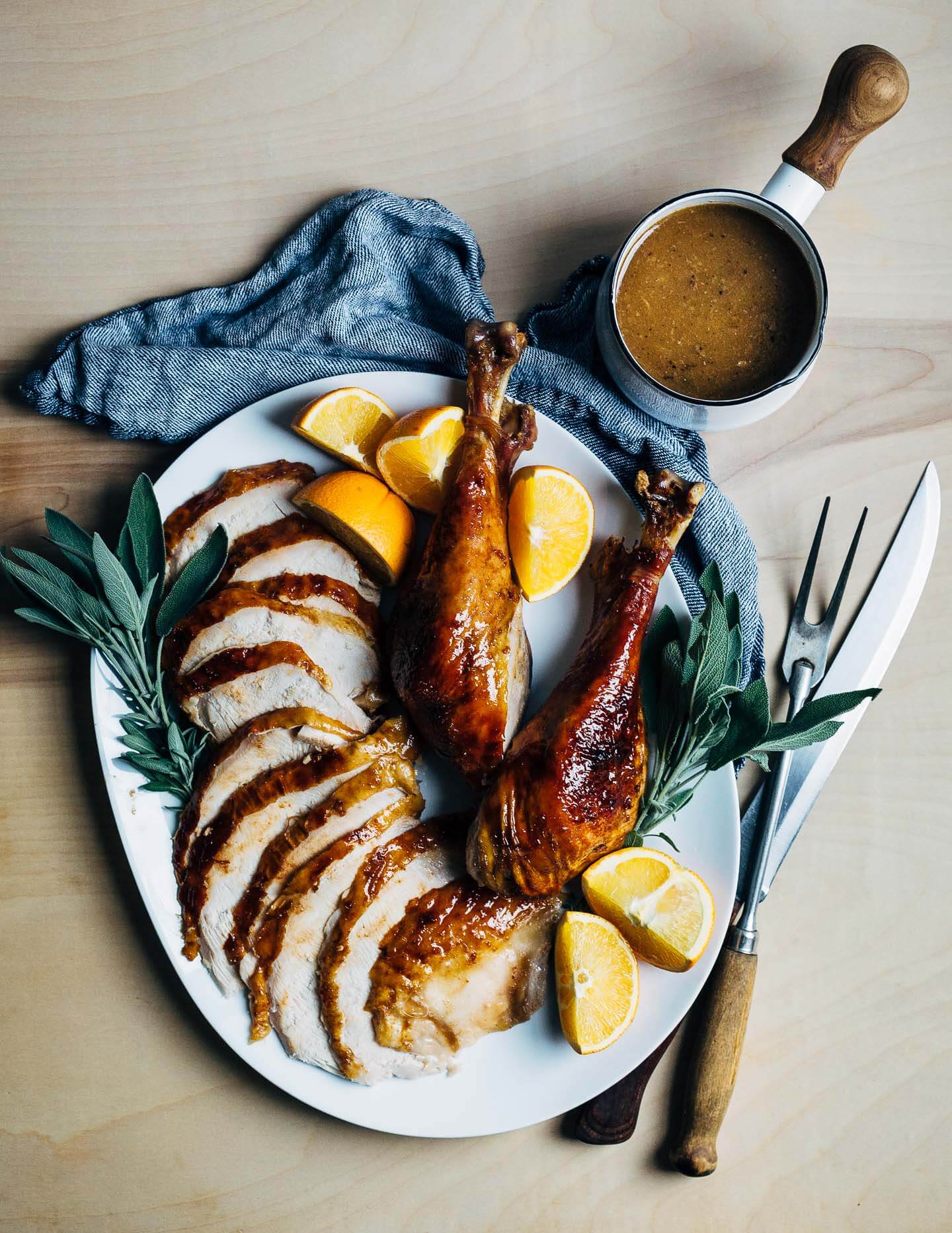 A platter with carved turkey meat and a pot of gravy alongside. 