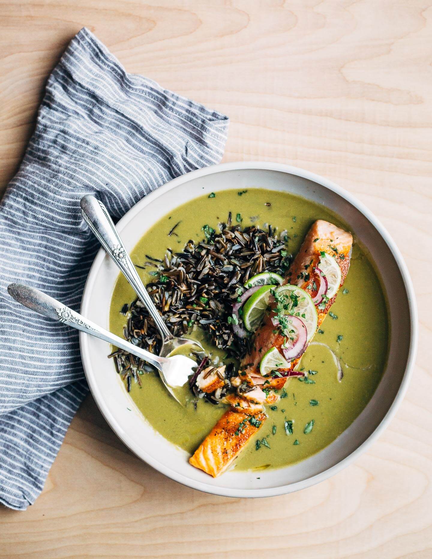 Nourishing green soup with creamy coconut milk and wild rice topped with a pan-seared salmon fillet.