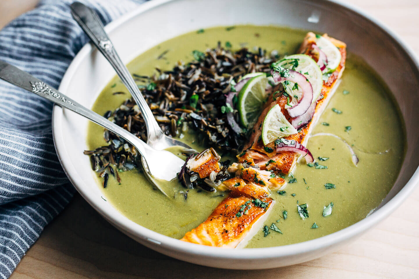 Nourishing green soup with creamy coconut milk and wild rice topped with a pan-seared salmon fillet.