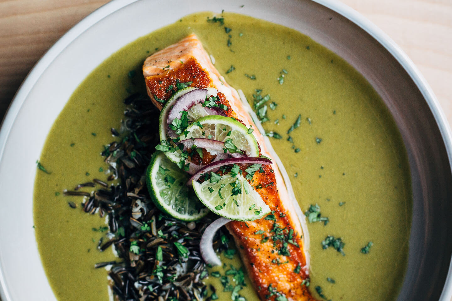 Nourishing green soup with creamy coconut milk and wild rice topped with a pan-seared salmon fillet.