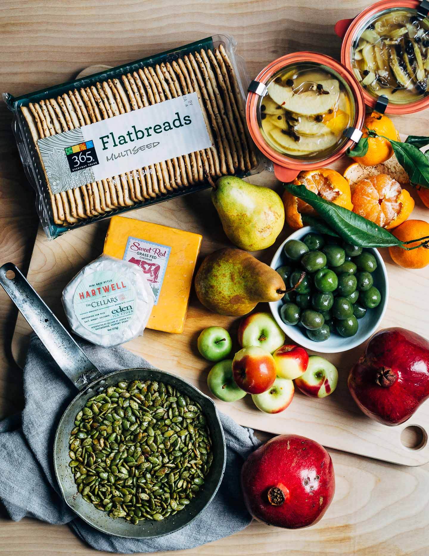 A modern holiday cheese board with red cheddar and brie-style cheeses, winter fruit, and sweet and sour quick-pickled apples.