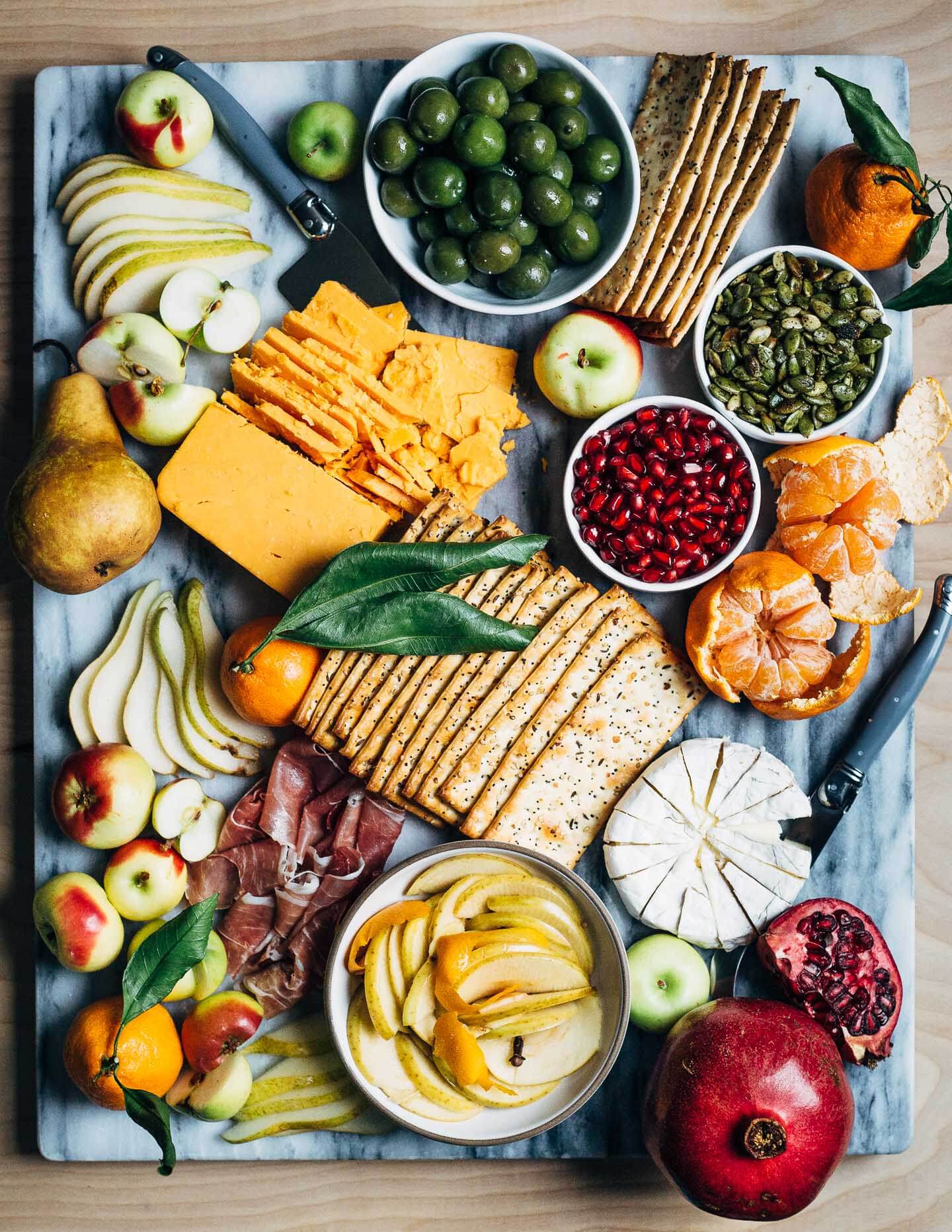 A modern holiday cheese board with red cheddar and brie-style cheeses, winter fruit, and sweet and sour quick-pickled apples. 
