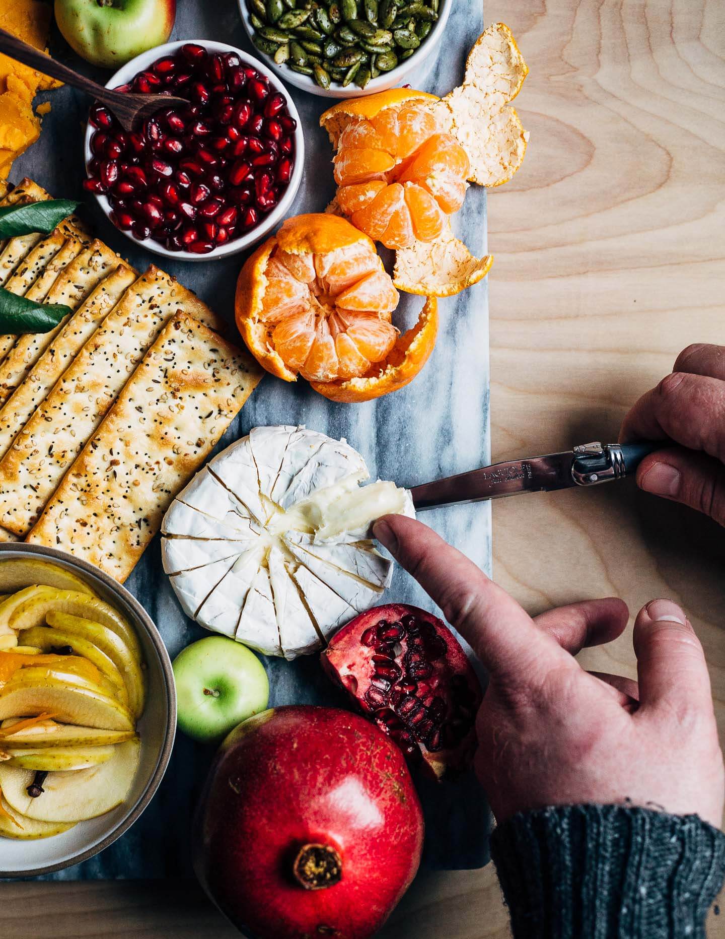 A modern holiday cheese board with red cheddar and brie-style cheeses, winter fruit, and sweet and sour quick-pickled apples.