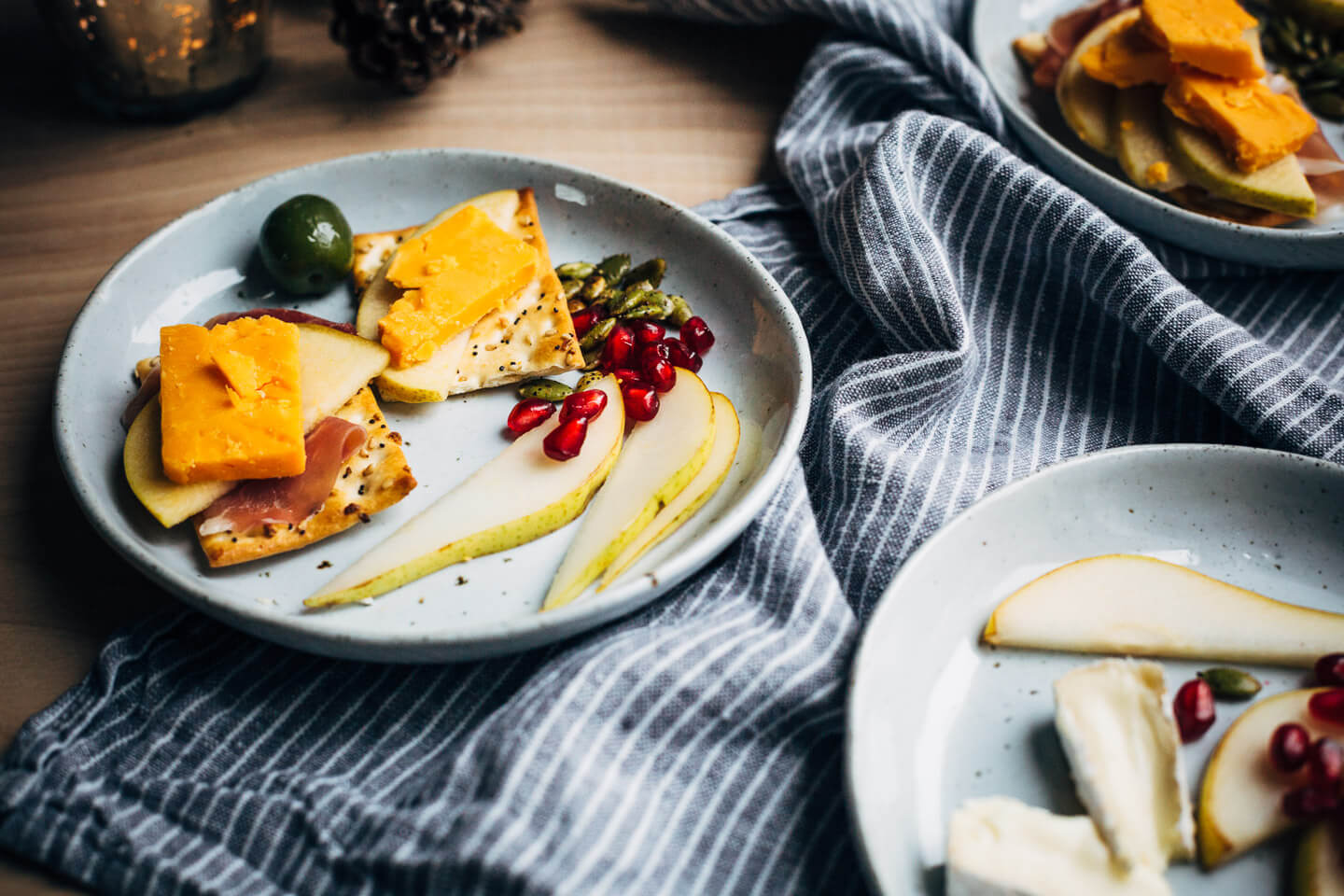 A modern holiday cheese board with red cheddar and brie-style cheeses, winter fruit, and sweet and sour quick-pickled apples.