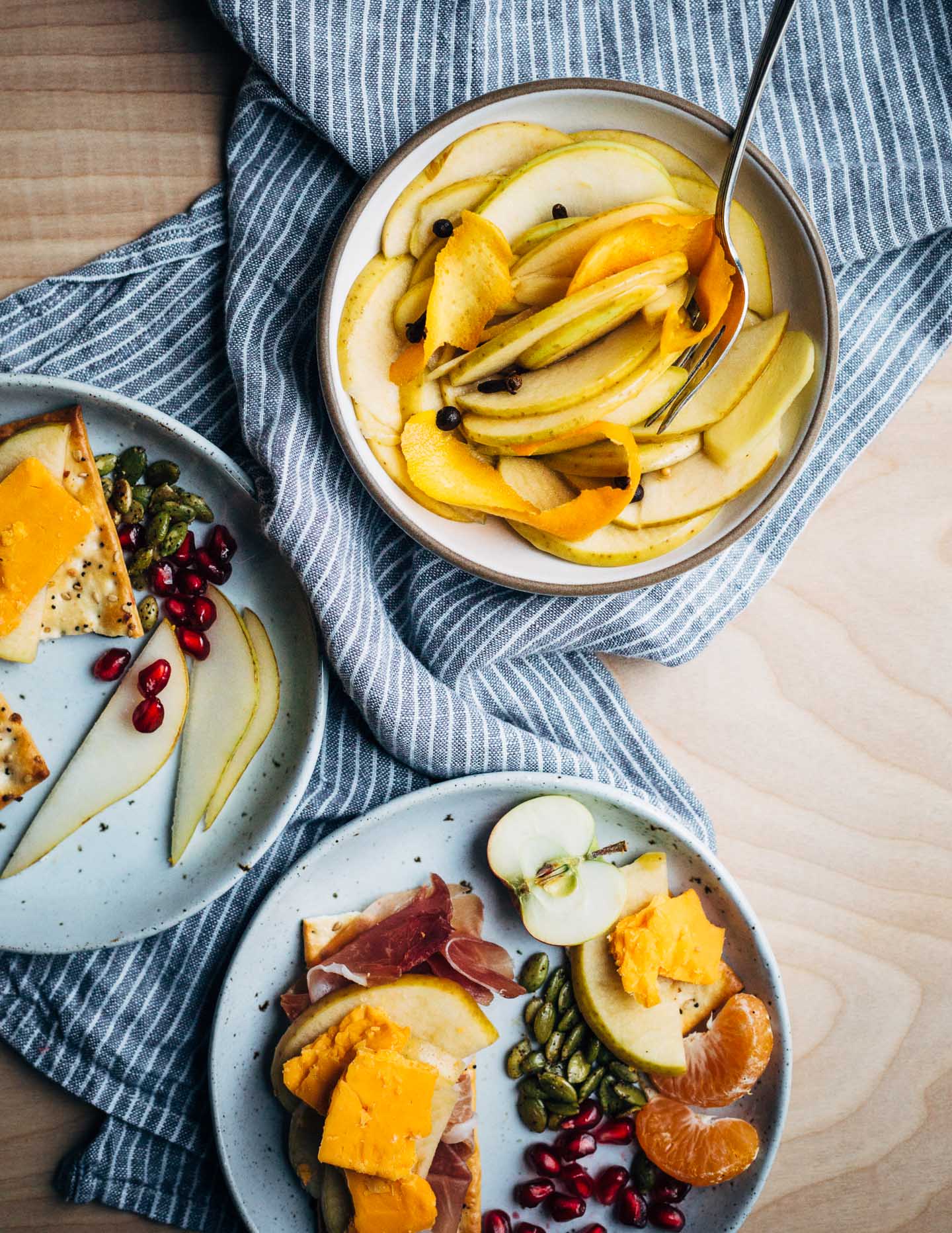 A modern holiday cheese board with red cheddar and brie-style cheeses, winter fruit, and sweet and sour quick-pickled apples.