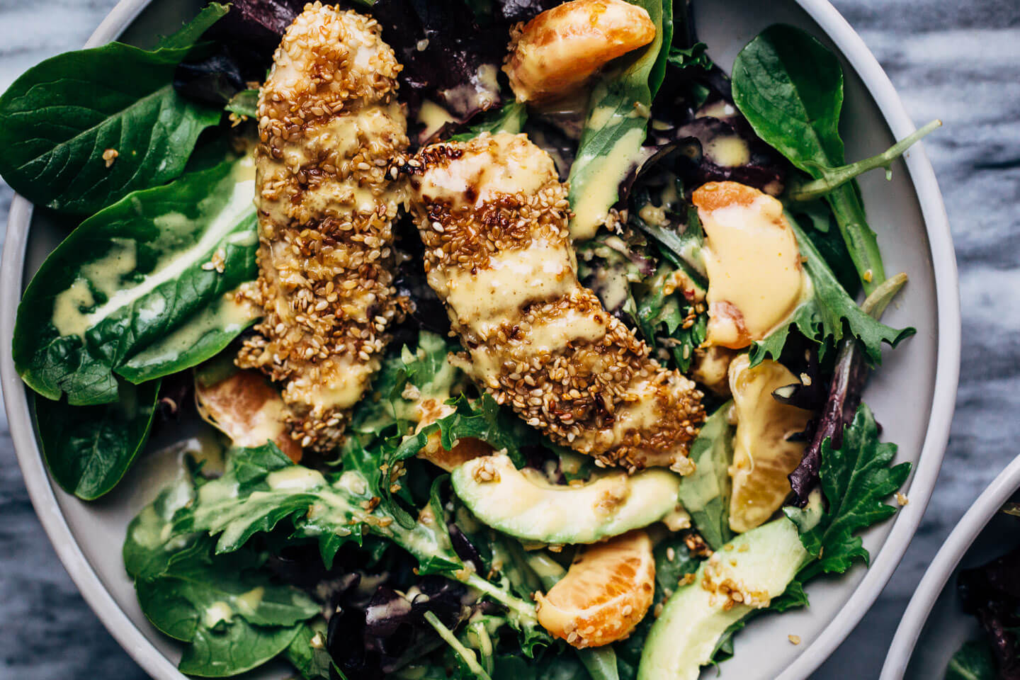 A healthful, Whole30-compliant avocado and mandarin orange salad topped with crisp sesame-crusted baked chicken tenders and drizzled with a creamy mandarin-ginger dressing.