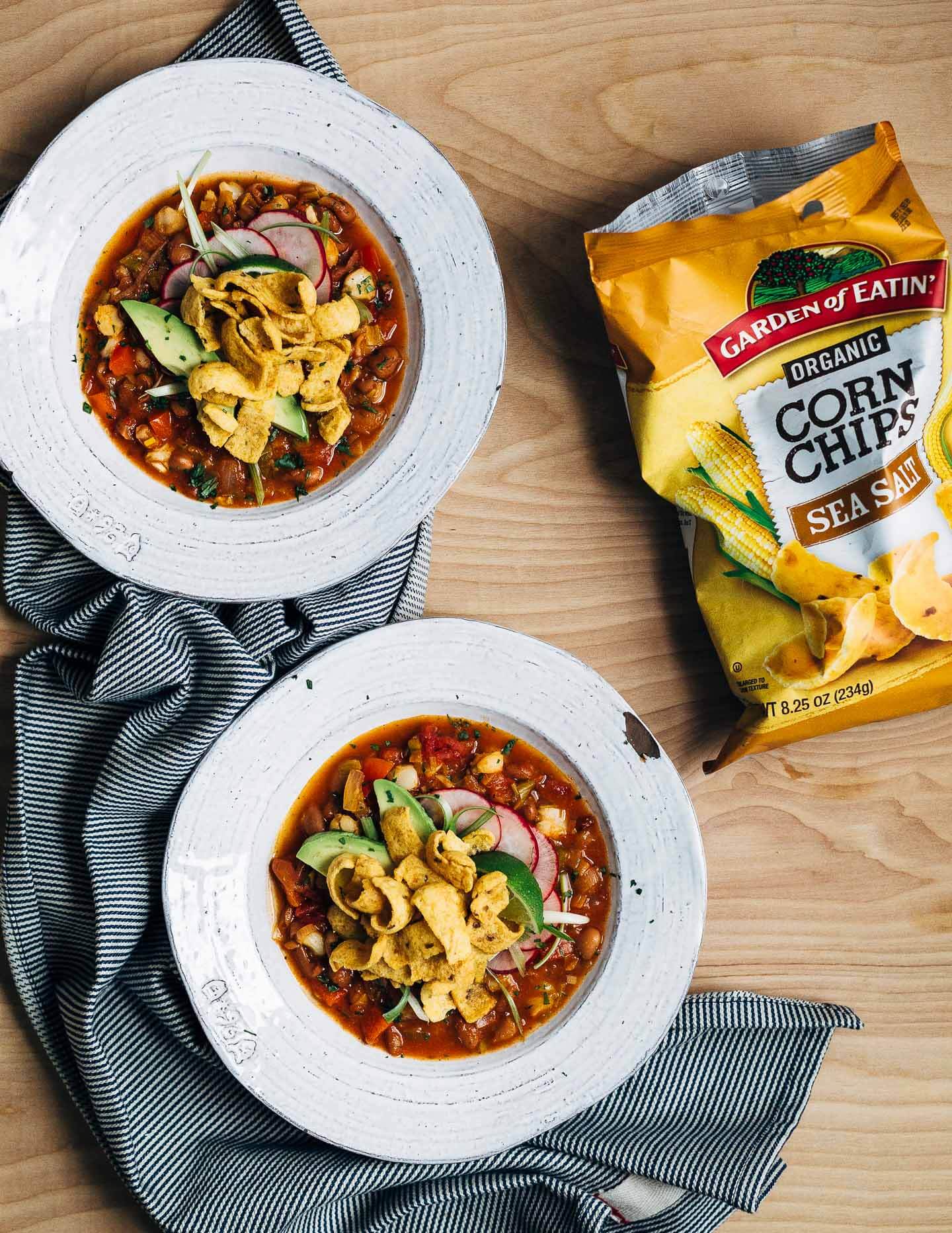 Hearty pinto bean chili with a flavorful tomato base flecked with leeks, chili peppers, and hominy and topped with fresh cilantro, lime, sliced avocado and radish, and crunchy corn chips. 