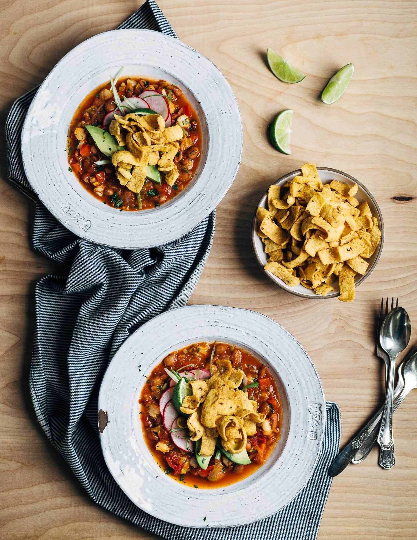 Hearty pinto bean chili with a flavorful tomato base flecked with leeks, chili peppers, and hominy and topped with fresh cilantro, lime, sliced avocado and radish, and crunchy corn chips.