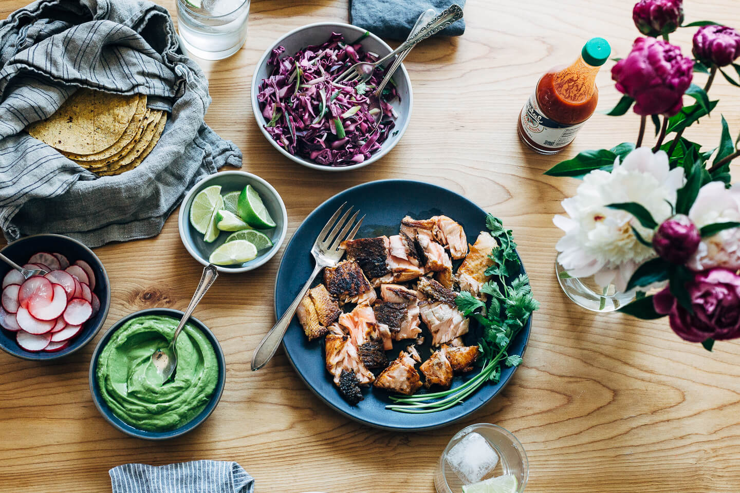 Spicy salmon tacos make for a delicious springtime feast. Tender, crisp skinned salmon is suffused with chipotle chili powder, cumin, and coriander, tucked into toothsome corn tortillas, and layered with a fennel and red cabbage slaw and an easy cilantro-avocado blender sauce. 