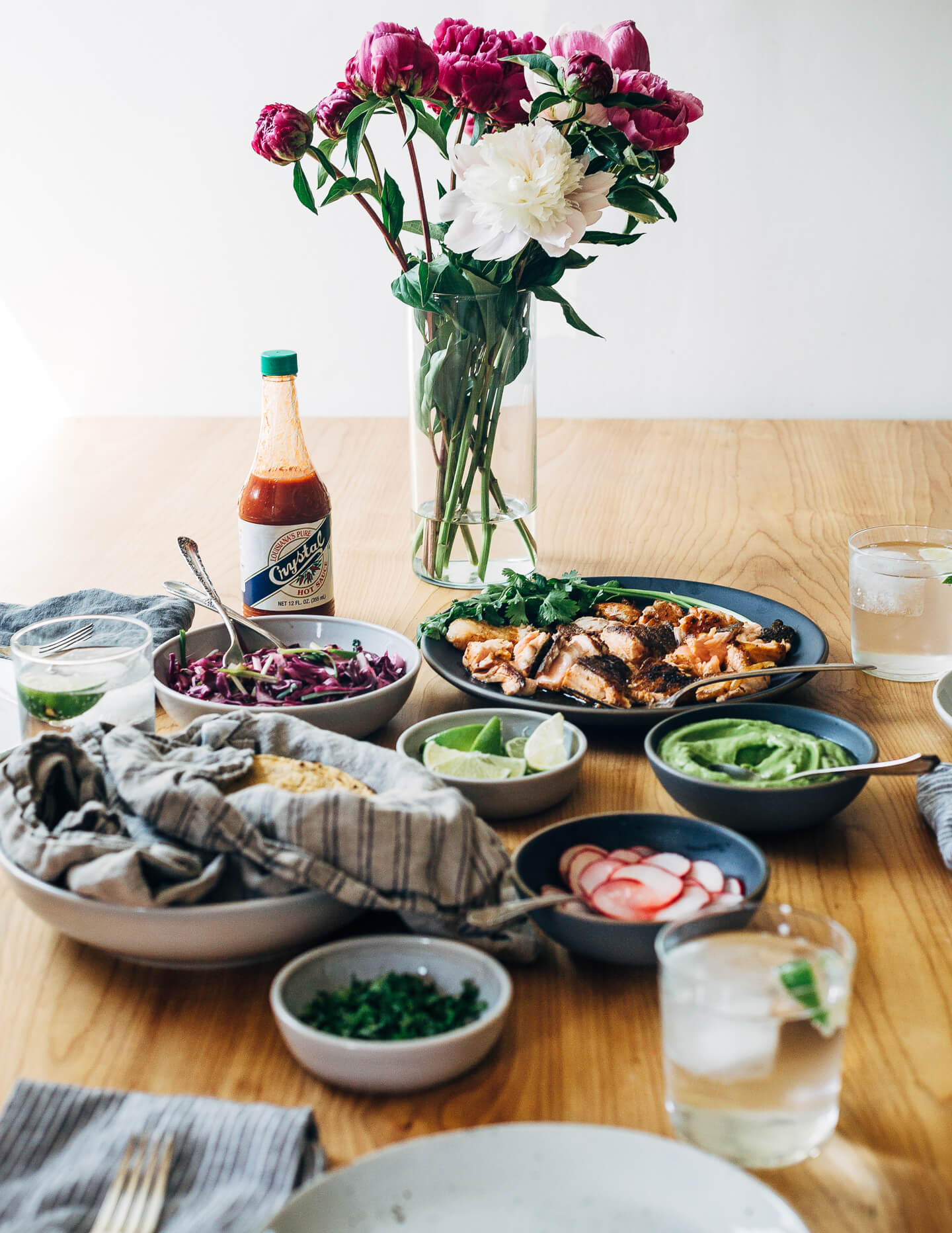 Spicy salmon tacos make for a delicious springtime feast. Tender, crisp skinned salmon is suffused with chipotle chili powder, cumin, and coriander, tucked into toothsome corn tortillas, and layered with a fennel and red cabbage slaw and an easy cilantro-avocado blender sauce. 