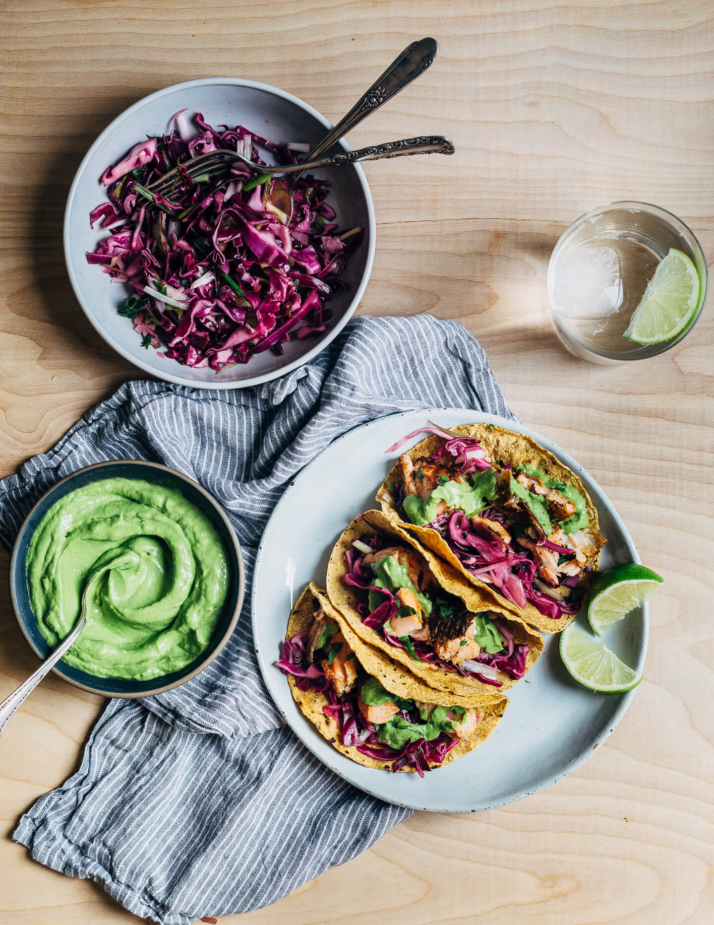 Spicy salmon tacos make for a delicious springtime feast. Tender, crisp skinned salmon is suffused with chipotle chili powder, cumin, and coriander, tucked into toothsome corn tortillas, and layered with a fennel and red cabbage slaw and an easy cilantro-avocado blender sauce. 