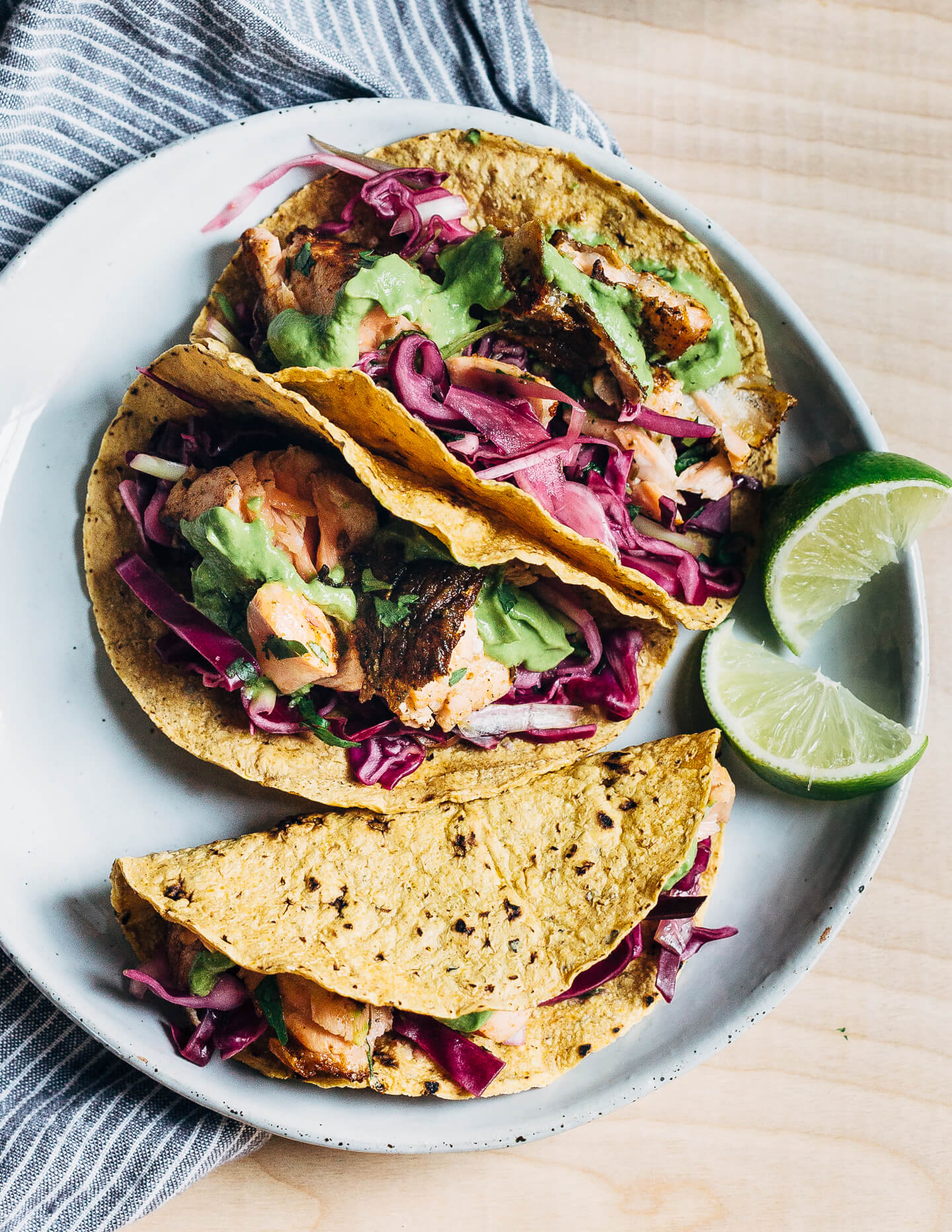 Spicy salmon tacos make for a delicious springtime feast. Tender, crisp skinned salmon is suffused with chipotle chili powder, cumin, and coriander, tucked into toothsome corn tortillas, and layered with a fennel and red cabbage slaw and an easy cilantro-avocado blender sauce. 