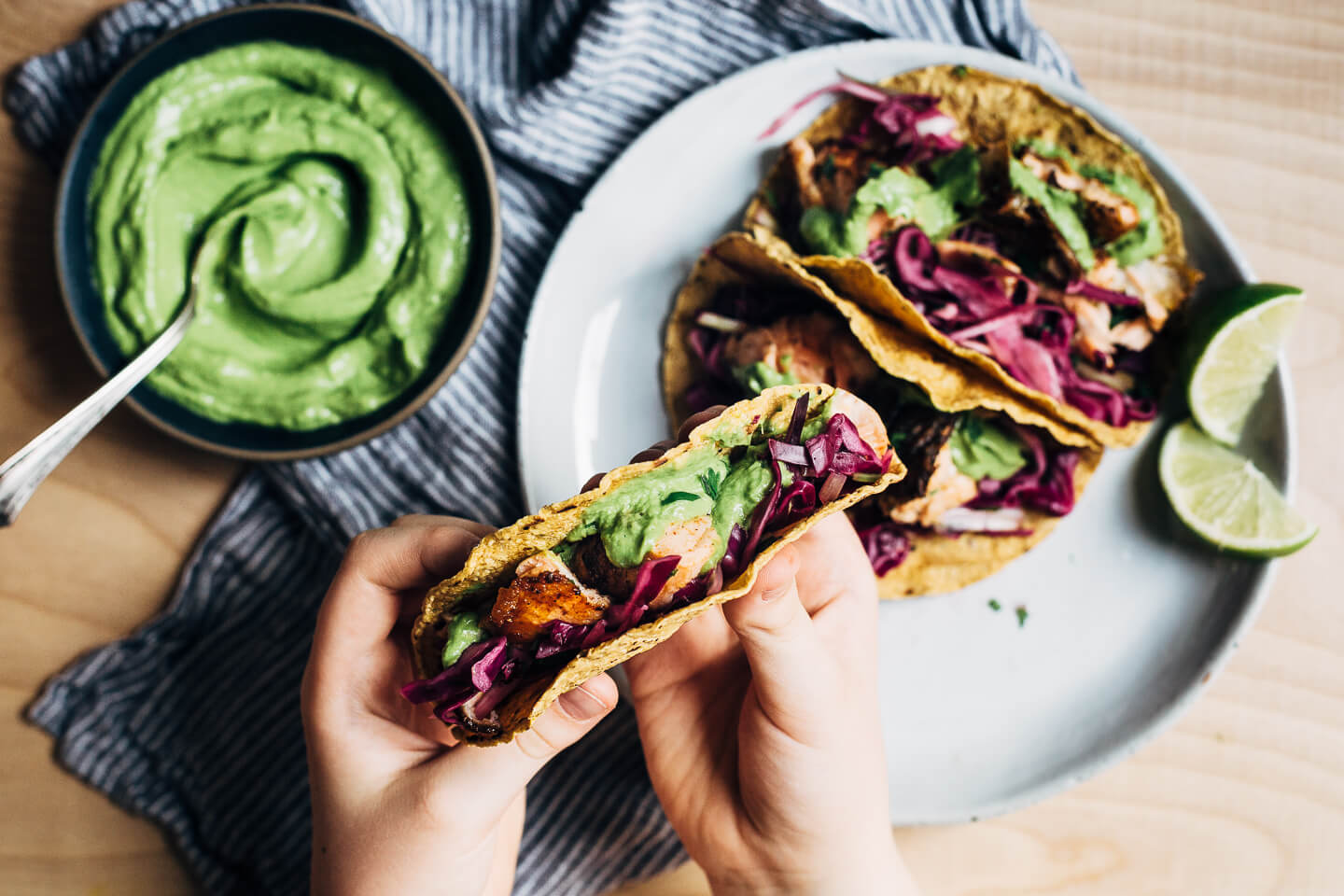 Spicy salmon tacos make for a delicious springtime feast. Tender, crisp skinned salmon is suffused with chipotle chili powder, cumin, and coriander, tucked into toothsome corn tortillas, and layered with a fennel and red cabbage slaw and an easy cilantro-avocado blender sauce. 