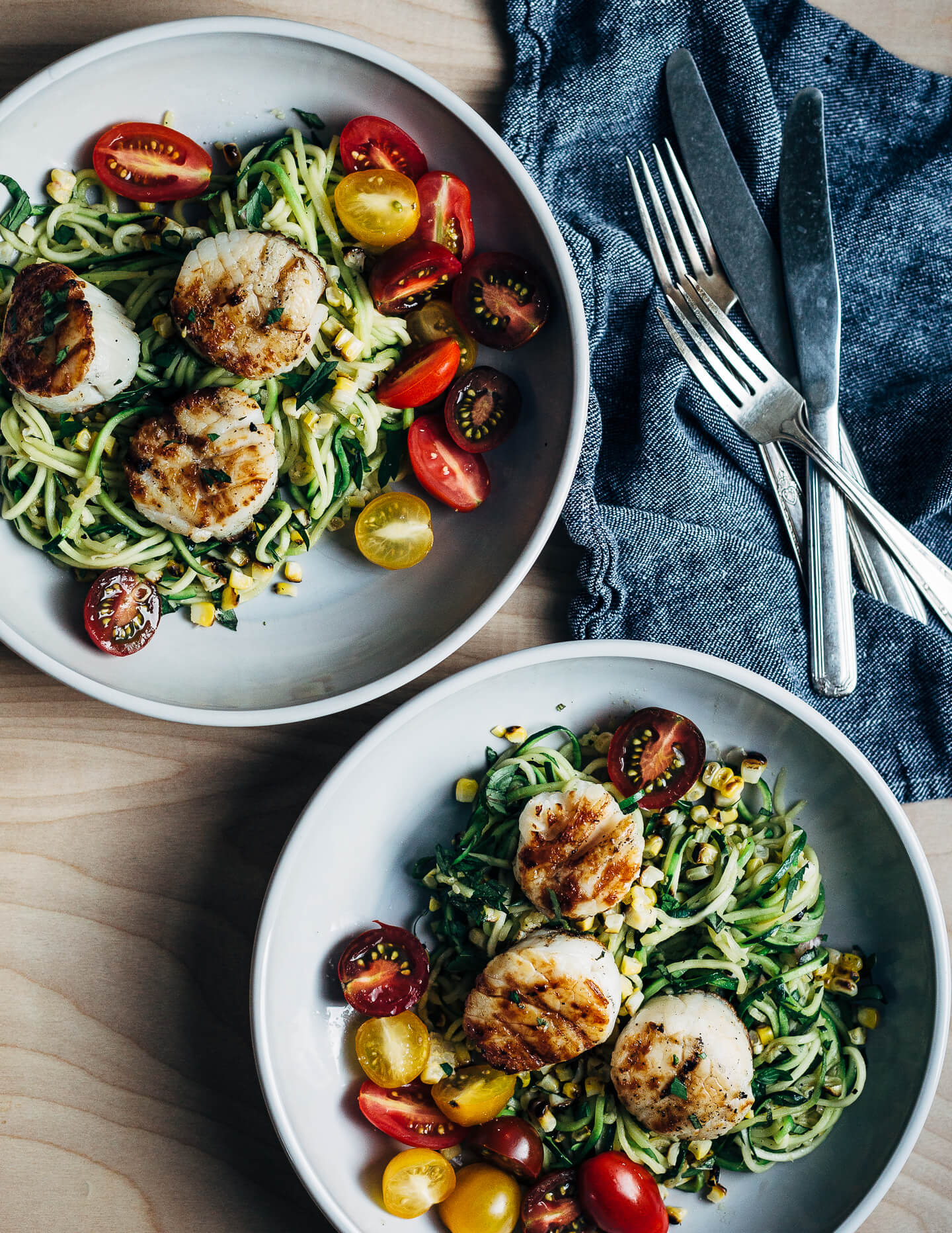 A simple grilled summer feast featuring grilled scallops served atop zucchini noodles tossed with charred corn and fresh herbs.