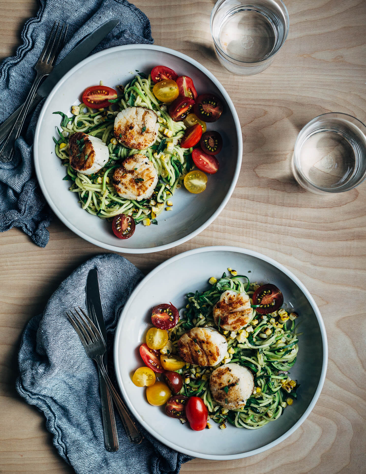 A simple grilled summer feast featuring grilled scallops served atop zucchini noodles tossed with charred corn and fresh herbs.