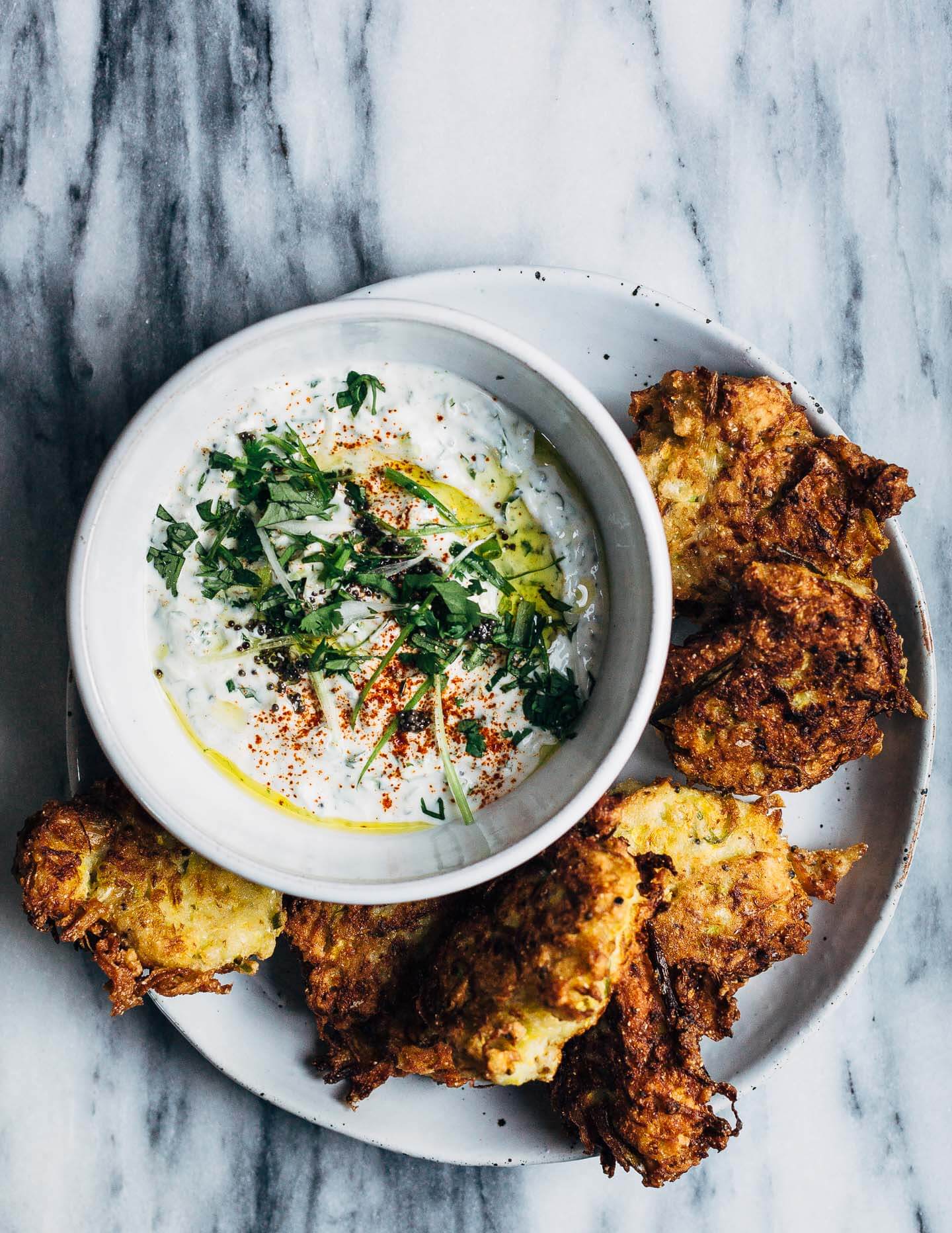A platter of fried summer squash fritters with a green onion raita dipping sauce