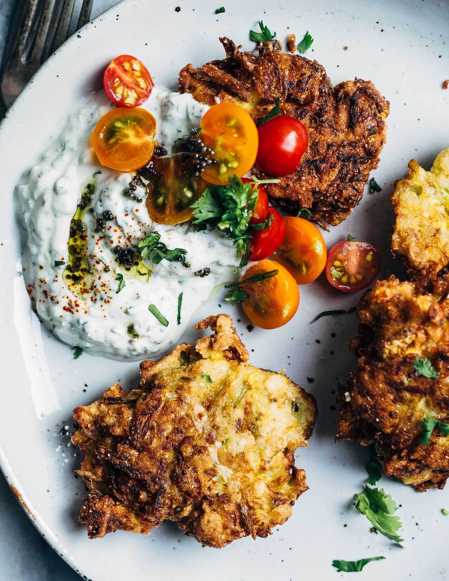 A close-up view of fritters with raita and cherry tomatoes. 