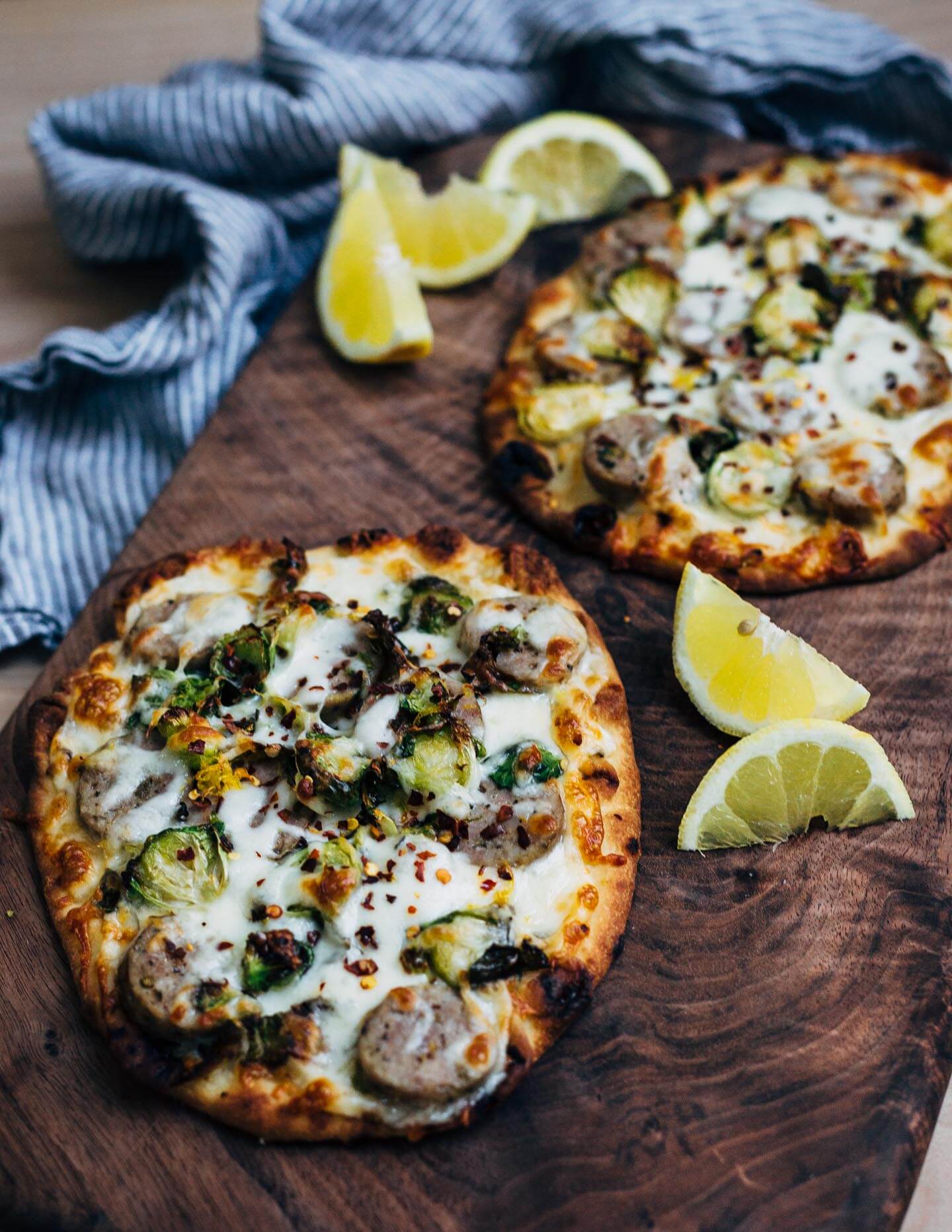 These sausage and Brussels sprout flatbread pizzas feature golden-edged roasted Brussels sprouts alongside tender sausage and melty mozzarella. Lemon zest and red pepper flakes punctuate the pizzas with brightness and heat, and lend a delightful complexity to this weeknight-friendly dish.