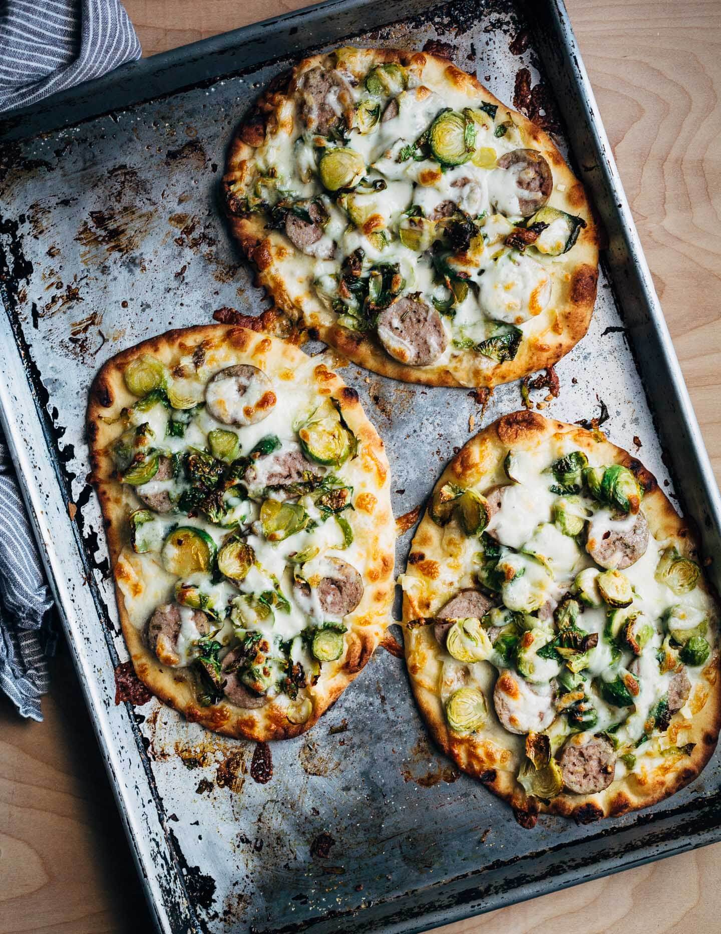 These sausage and Brussels sprout flatbread pizzas feature golden-edged roasted Brussels sprouts alongside tender sausage and melty mozzarella. Lemon zest and red pepper flakes punctuate the pizzas with brightness and heat, and lend a delightful complexity to this weeknight-friendly dish.