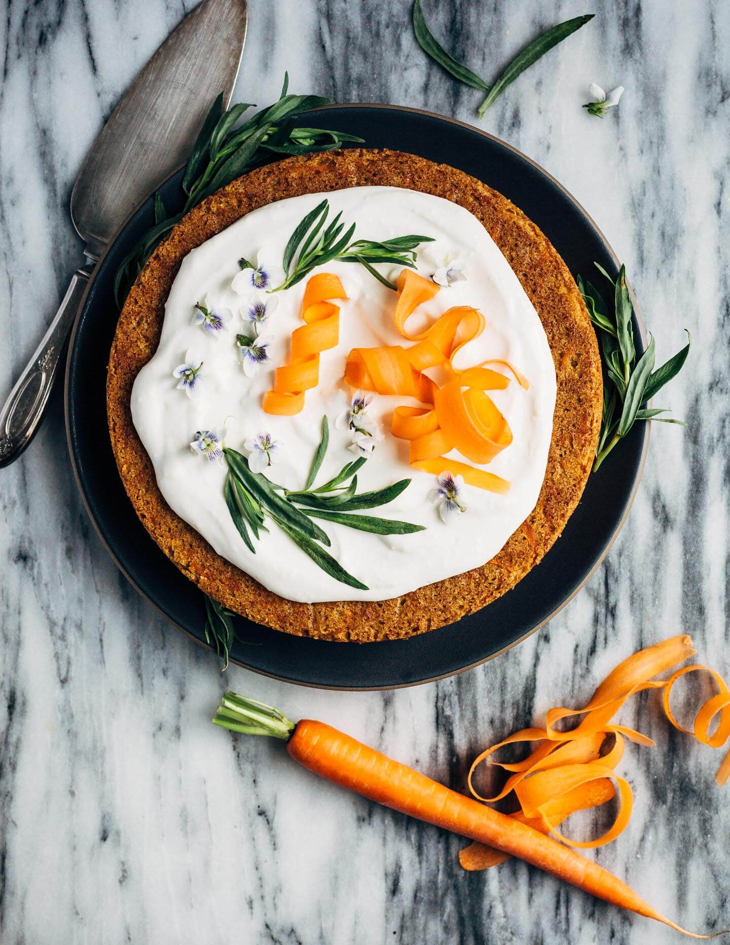 A simple olive oil carrot cake for spring celebrations! The tender, springy whole wheat crumb is suffused with nutty olive oil, fresh carrots, and orange zest. The cake is topped with an airy, lightly sweet yogurt and cream cheese frosting, carrot ribbons, tarragon, and edible flowers. 