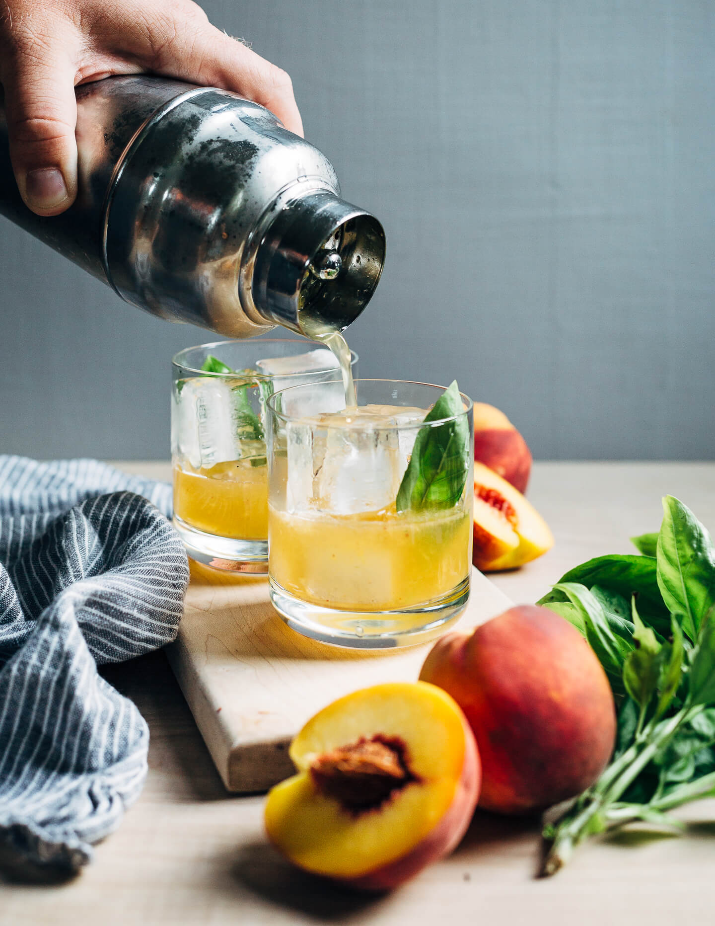 Straining a peach bourbon smash cocktail into ice-filled cocktail glasses. 