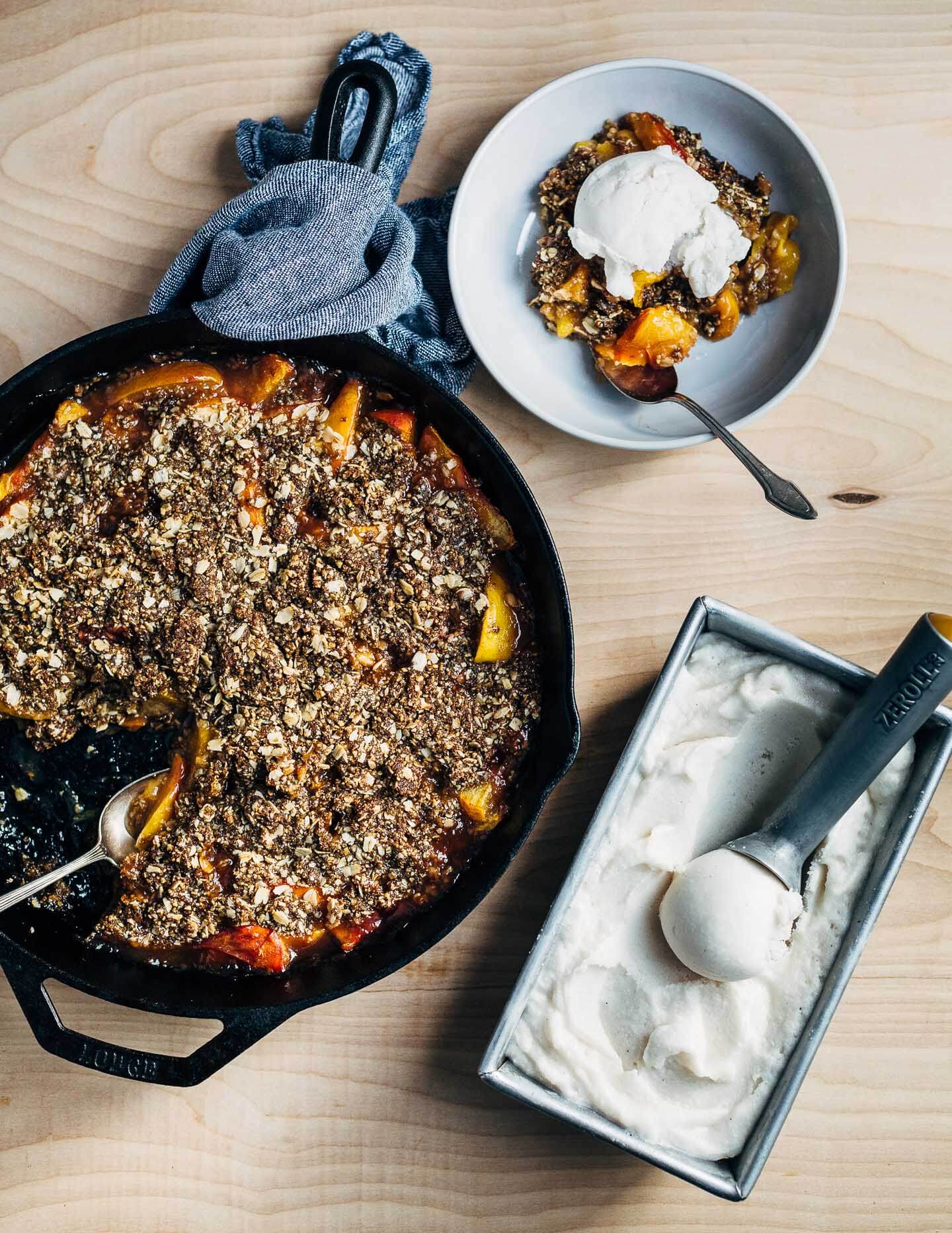 This intensely flavorful gluten-free, vegan peach crumble with masala chai-spiced coconut sorbet is the perfect summer baking project. Big flavors like cardamom, ginger, and cinnamon lend zip to creamy homemade coconut sorbet – an ideal counterpoint to chewy, molasses-infused seed and oat crumbles and bright peaches baked with a host of fragrant spices.
