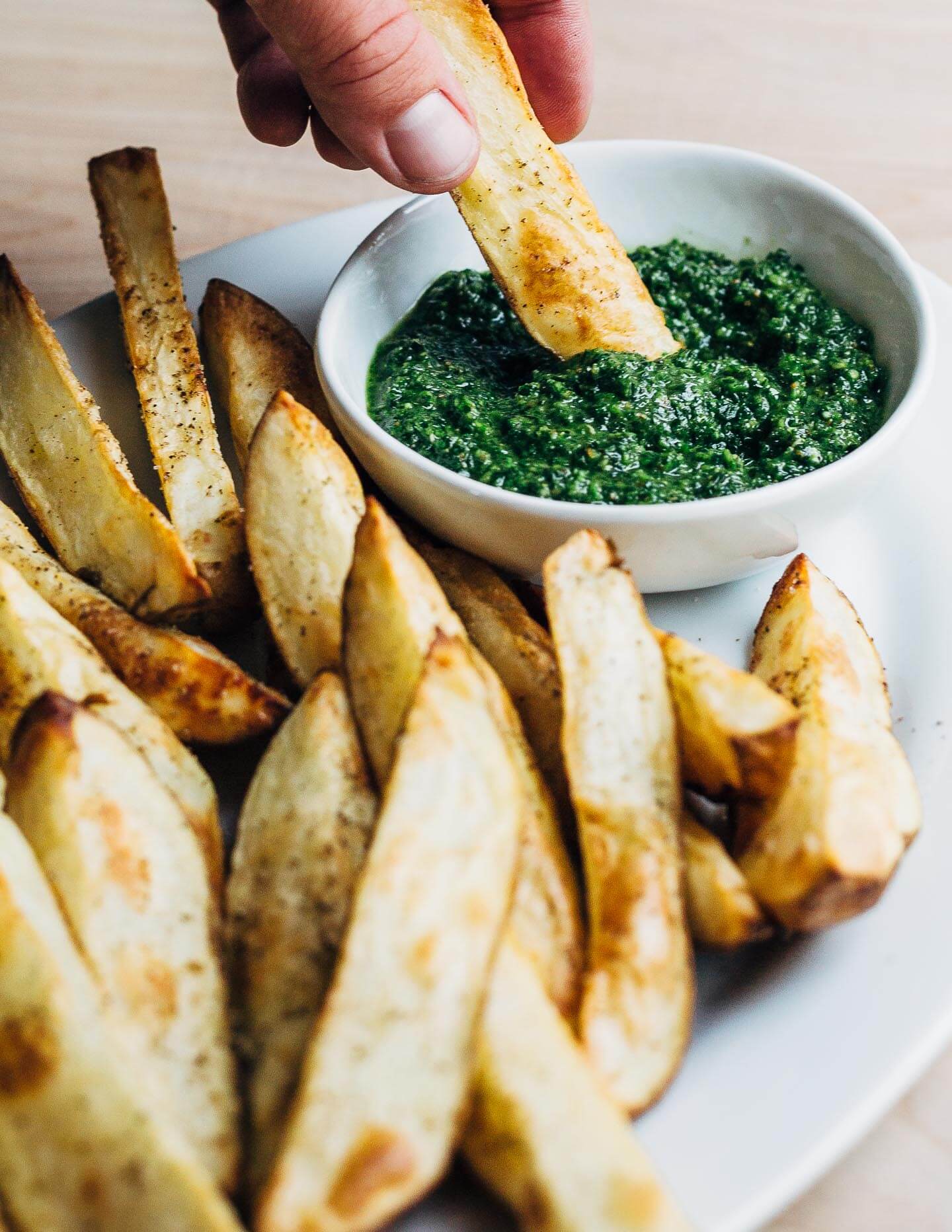 Dipping a crisp roasted potato wedge into a small dish of homemade zhug. 