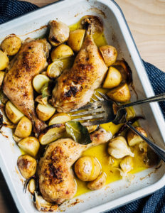 A roasting pan with chicken legs and potatoes.