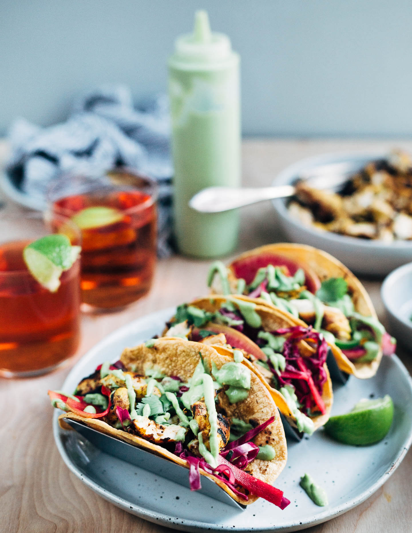 These quick and easy grilled chicken tacos start with a vibrant orange and lime juice marinade, and are layered with avocado-lime sauce, and a simple red cabbage and radish slaw.