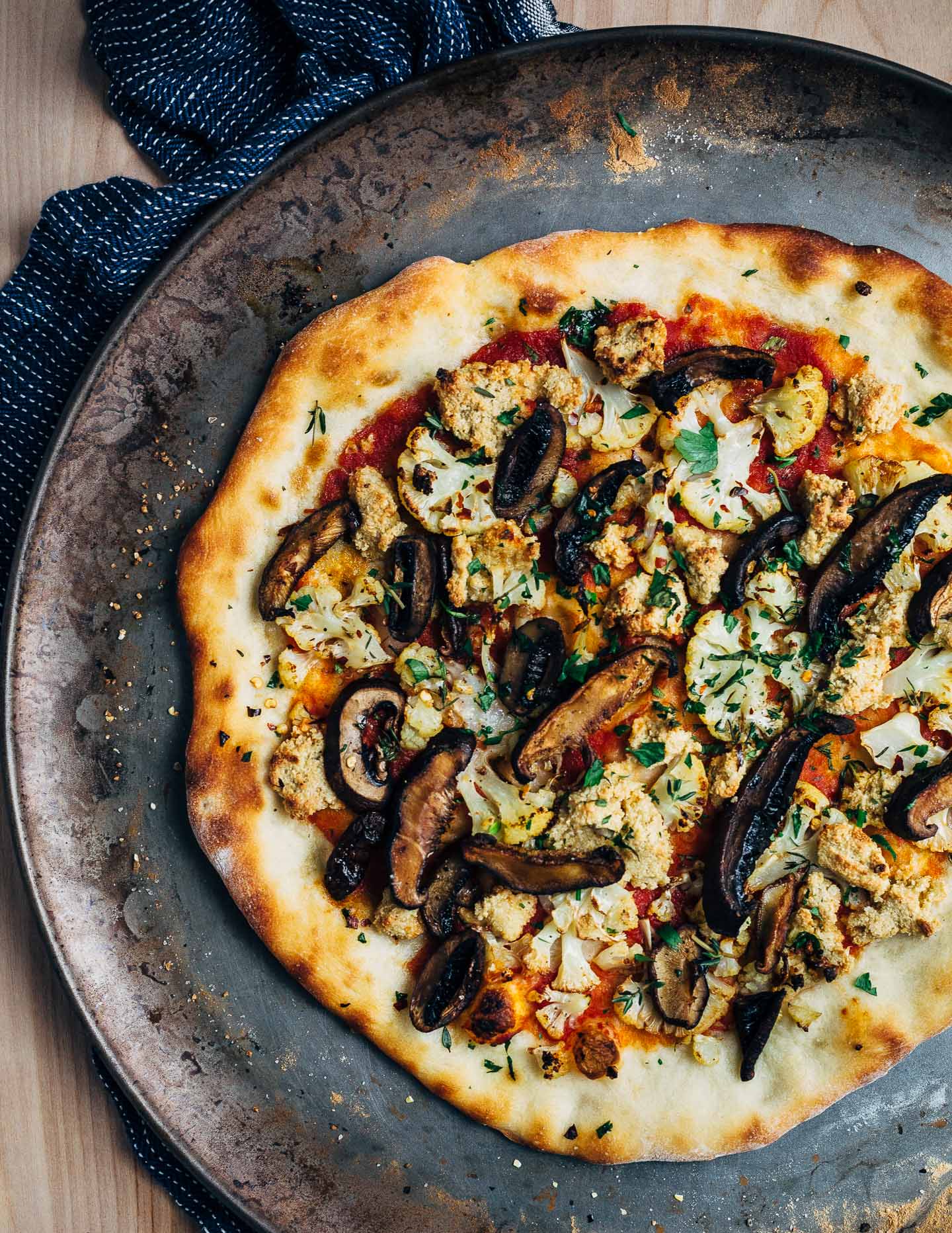 A super flavorful vegan pizza recipe featuring roasted cauliflower and mushrooms, fresh herbs, and a sunflower seed-nutritional yeast topping.