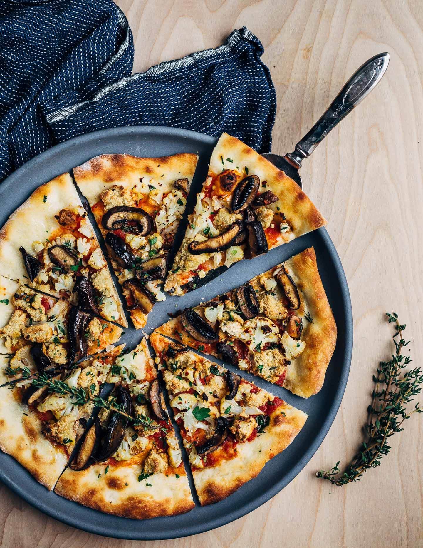 A super flavorful vegan pizza recipe featuring roasted cauliflower and mushrooms, fresh herbs, and a sunflower seed-nutritional yeast topping.
