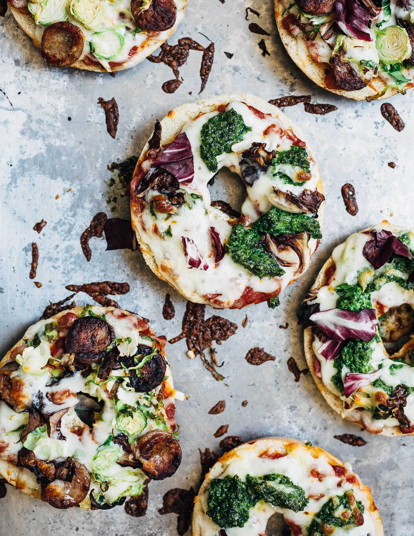 How to make pizza bagels at home! Customize your pizza bagels with pesto, sausage, greens, or whatever vegetables and toppings you have on hand.