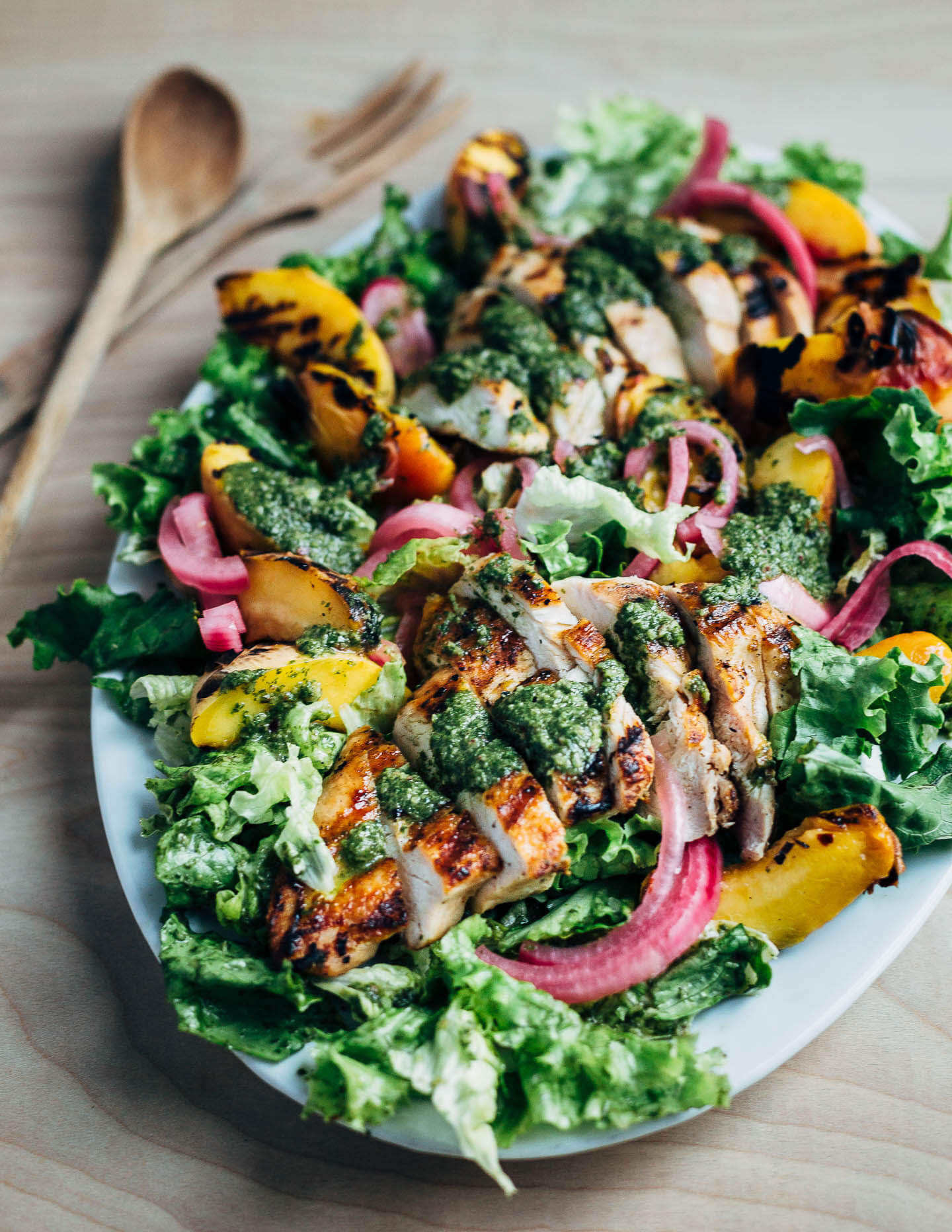 A colorful, summer-inspired grilled chicken and peach salad, pickled onions, greens, and basil vinaigrette.