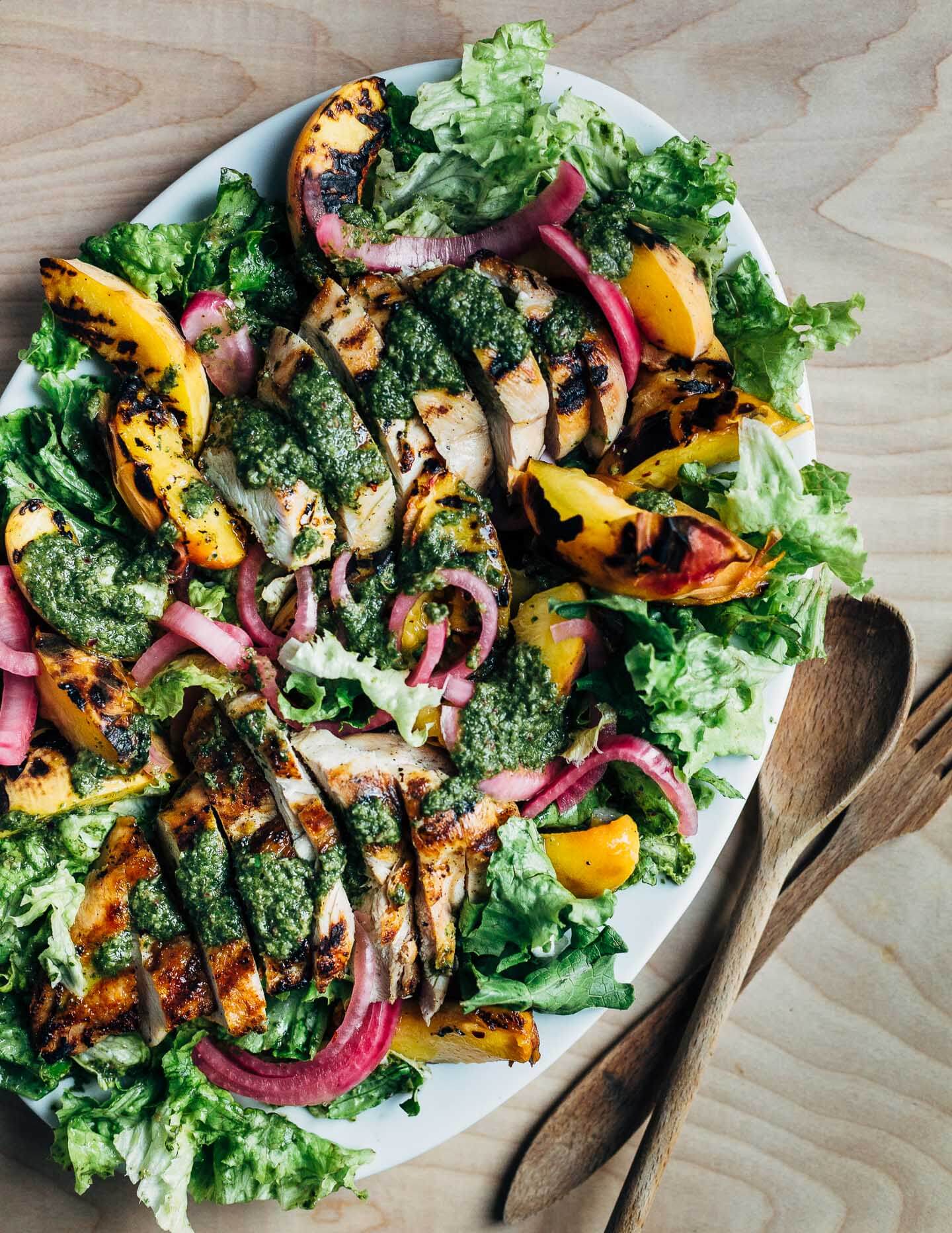 A colorful, summer-inspired grilled chicken and peach salad, pickled onions, greens, and basil vinaigrette.