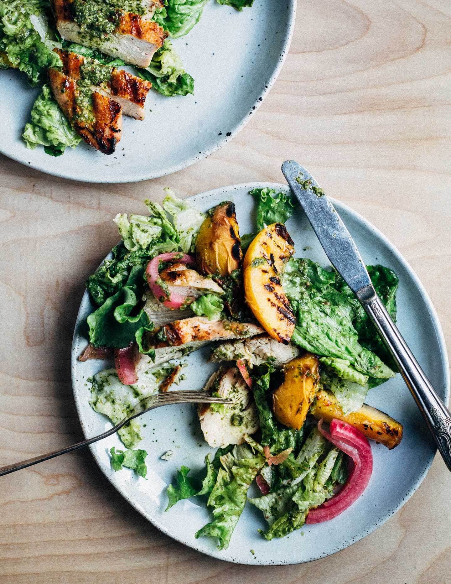 A colorful, summer-inspired grilled chicken and peach salad, pickled onions, greens, and basil vinaigrette.