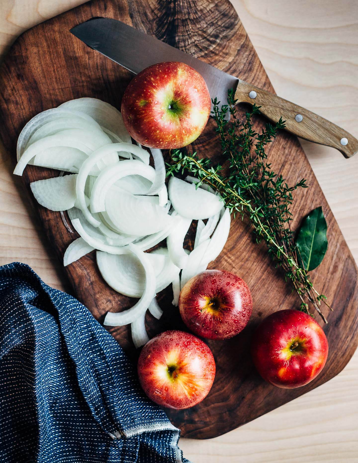 Apples, onions, and herbs on a cutting board. 