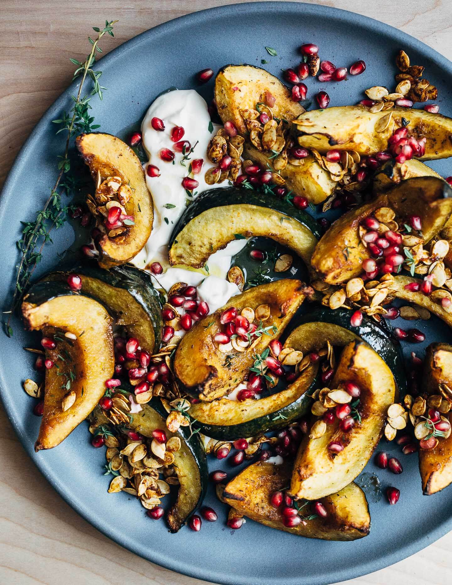 Sweet and savory roasted acorn squash wedges tossed with brown sugar, spicy paprika, black pepper, and fresh thyme. The squash is served with a dollop of crème fraîche, toasted squash seeds, and pomegranate arils.