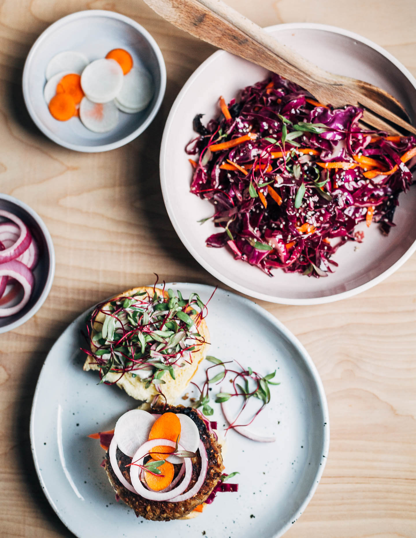 Tahini veggie burgers topped with quick pickles and microgreens, and a red cabbage slaw. 