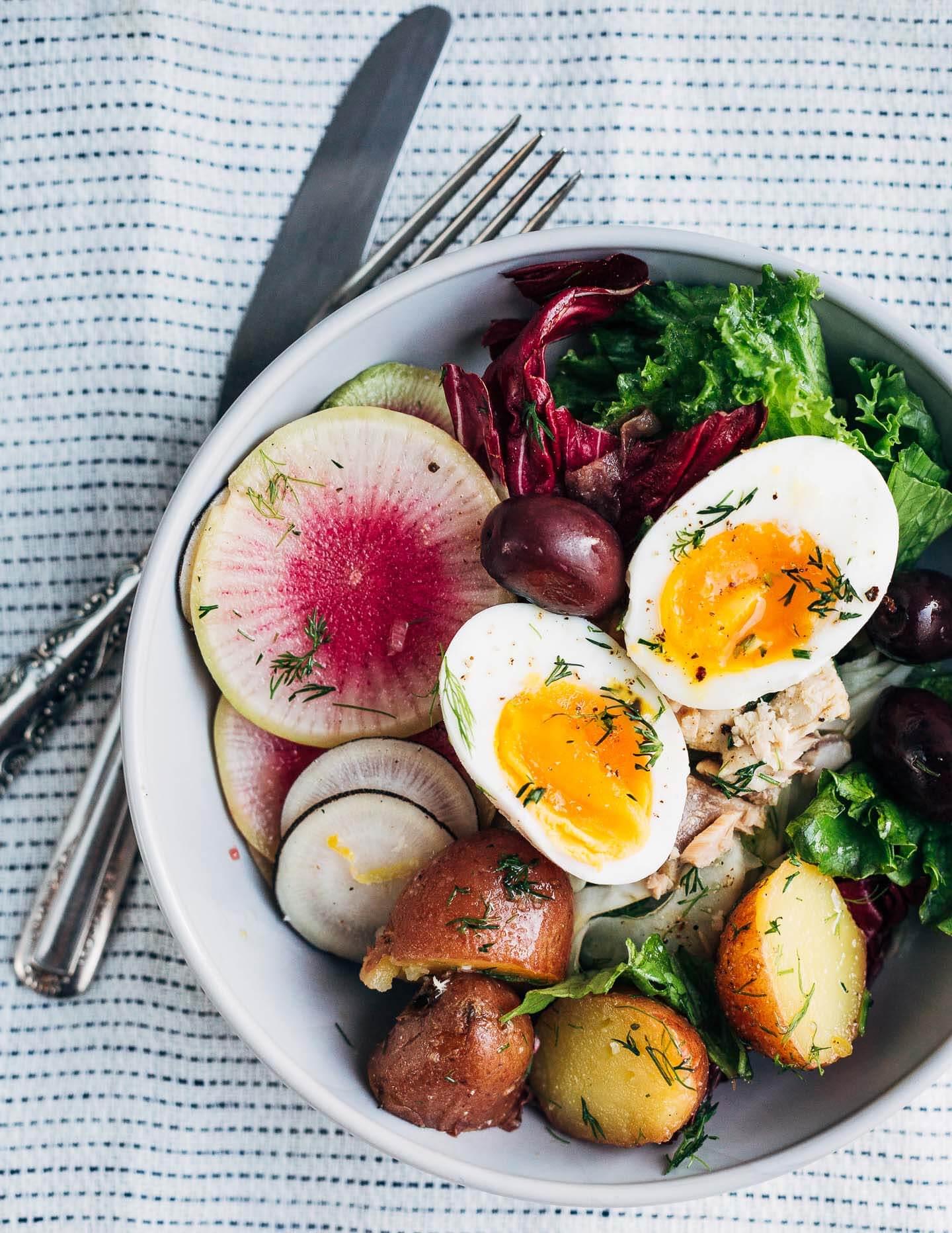 This winter Nicoise-ish salad hits all the right notes with crunchy shaved fennel and radishes, greens and radicchio, tender new potatoes suffused with herbs and a punchy vinaigrette, just-set 7-minute steamed eggs, and piles of olives.