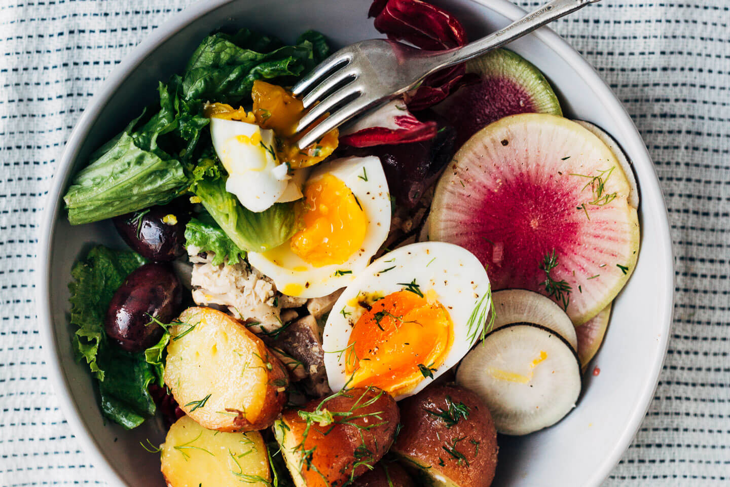 This winter Nicoise-ish salad hits all the right notes with crunchy shaved fennel and radishes, greens and radicchio, tender new potatoes suffused with herbs and a punchy vinaigrette, just-set 7-minute steamed eggs, and piles of olives.