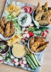 This vibrant chicken tenders board features juicy oven-baked chicken tenders in three delicious flavor profiles: garlic and herb with yogurt ranch, sesame-ginger with a sweet and sour dipping sauce, and classic honey mustard with a spicy sweet Dijon dipping sauce.